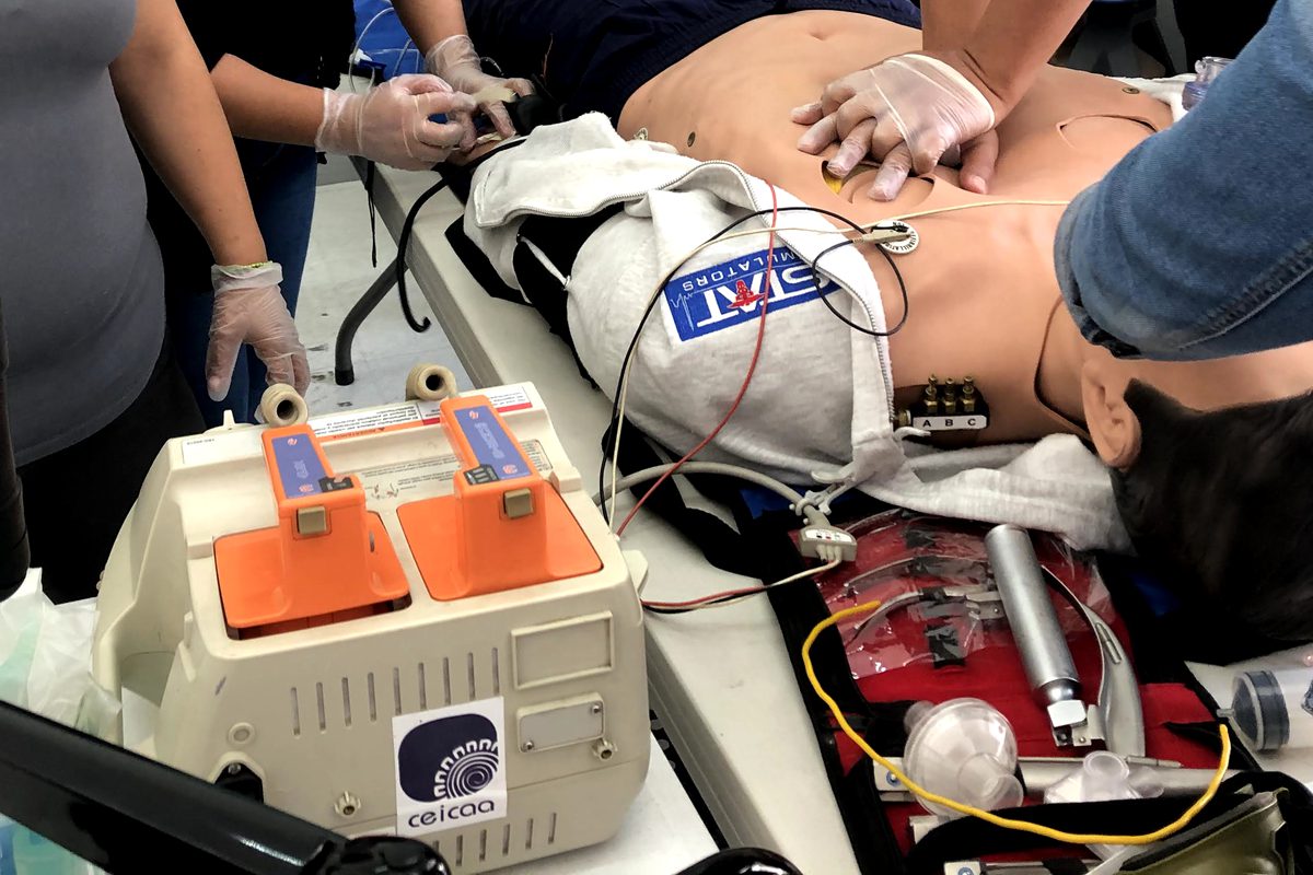 Megacódigo en un simulador de paciente: compresiones torácicas con guantes, monitor desfibrilador de CEICAA y equipo de vía aérea.