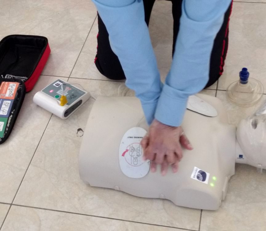 Compresiones torácicas en un maniquí de adulto, con el DEA de entrenamiento al lado.