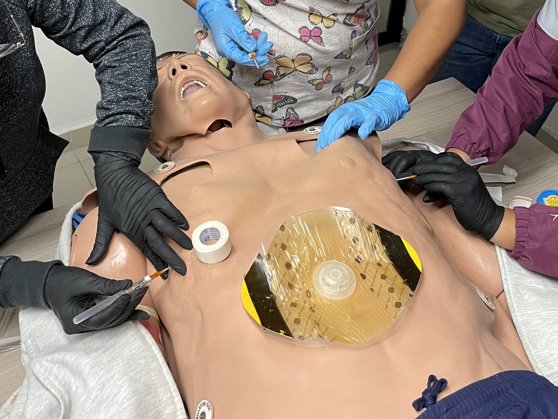 Práctica de trauma en un simulador: sello torácico en el tórax y manos con guantes trabajando sobre el maniquí.