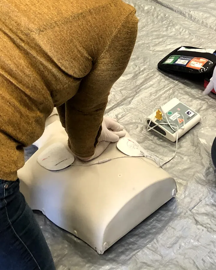 Compresiones torácicas con guantes en un maniquí con los parches del DEA de entrenamiento conectados.