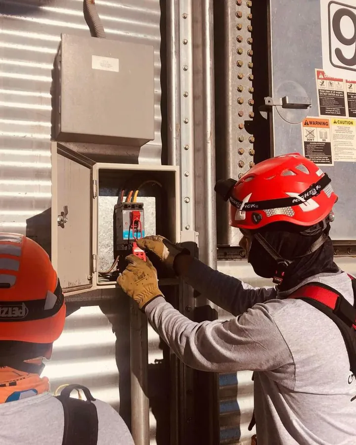 Rescatista con casco rojo y el rostro cubierto coloca un candado de bloqueo en el tablero eléctrico de un silo.