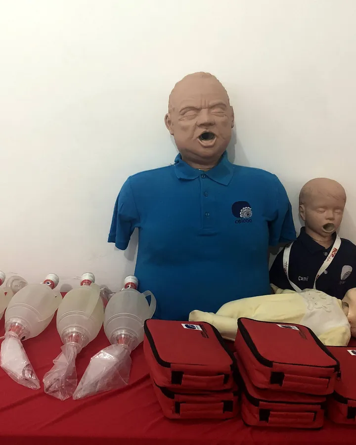 Maniquíes de adulto, niño y lactante con bolsas-válvula-mascarilla sobre una mesa roja.