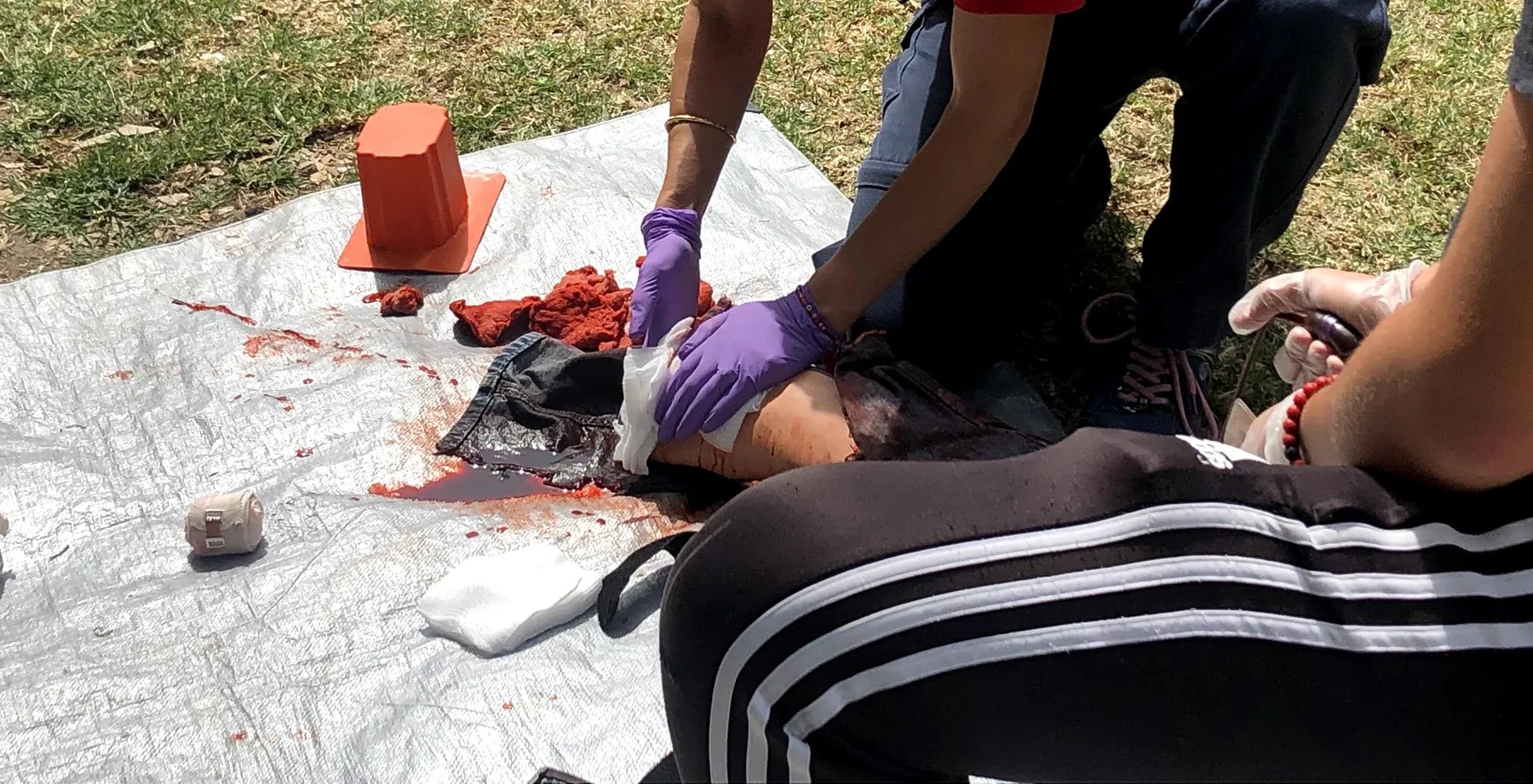 Empaquetamiento de una herida: manos con guantes morados meten gasa en el simulador para controlar el sangrado.