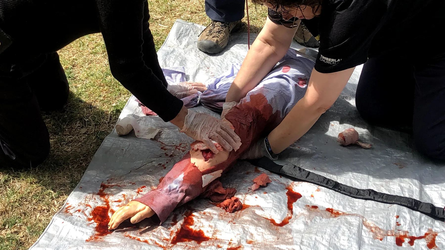 Control de una hemorragia en un simulador de brazo amputado, sobre una lona al aire libre.