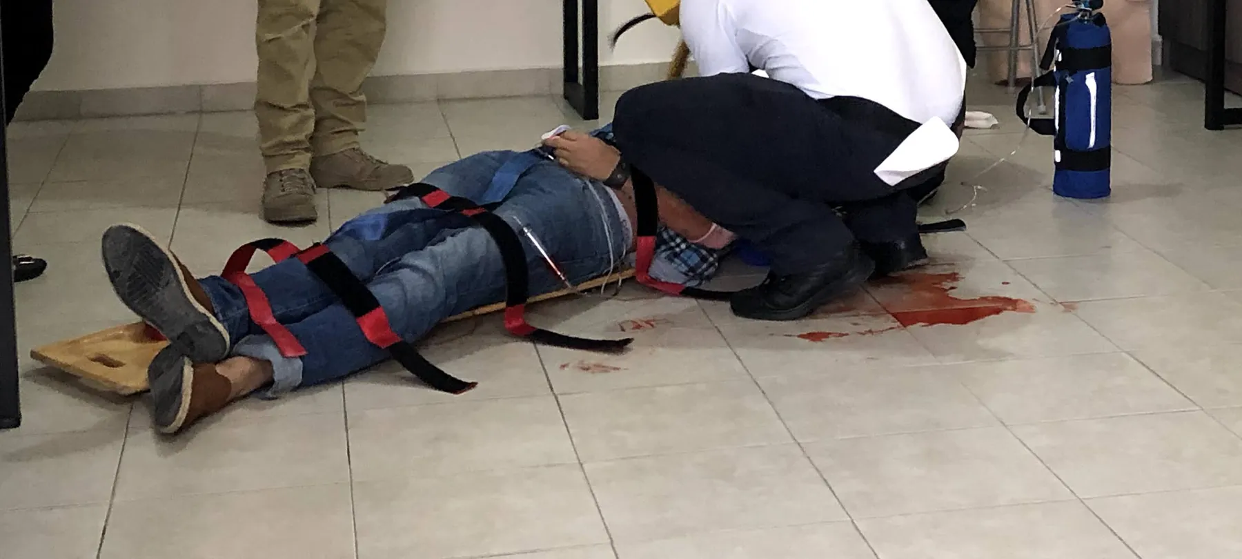 Escenario de trauma en el aula: un paciente simulado, sujeto con correas a una tabla espinal, mientras el equipo lo atiende junto al oxígeno.