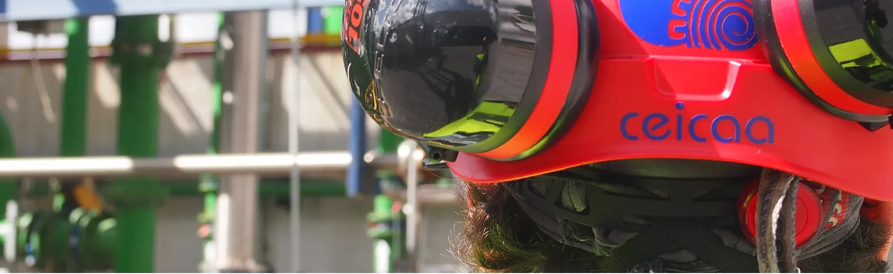 Casco rojo de rescate con la palabra «ceicaa», visto de cerca sobre una planta industrial.