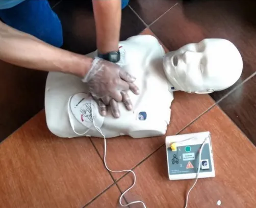 Manos con guantes dan compresiones a un maniquí conectado a un desfibrilador de entrenamiento.