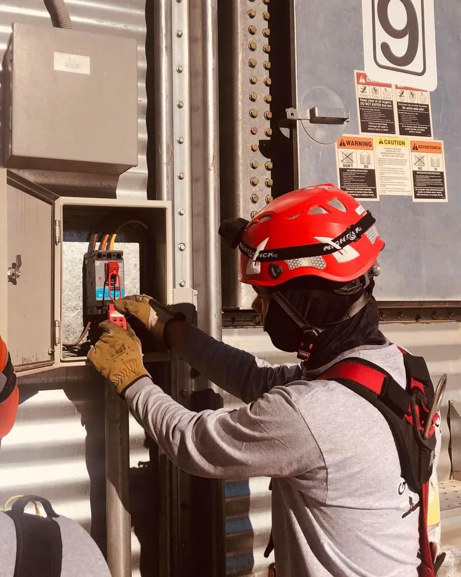 Rescatista con casco rojo y el rostro cubierto coloca un candado de bloqueo en el tablero eléctrico de un silo.
