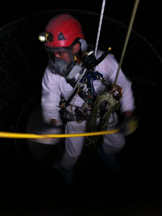 Rescatista con traje blanco, máscara y casco con lámpara dentro de un espacio confinado, de noche.