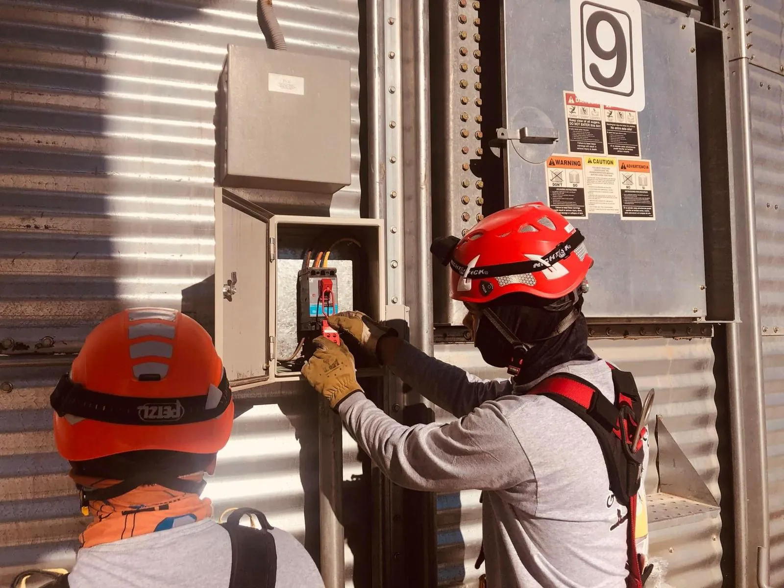 Dos rescatistas con casco y el rostro cubierto colocan un candado de bloqueo en el tablero eléctrico de un silo.